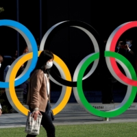 Women walk past the Olympic rings in front of the Japan Olympics Museum in March 2020. | REUTERS