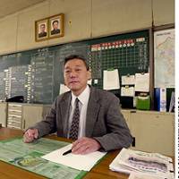 School Principal Song Hyong Jin poses at his desk in the teachers\' room, with the portraits of North Korean leaders behind him. | PHOTOS COURTESY OF PARCO THEATRE