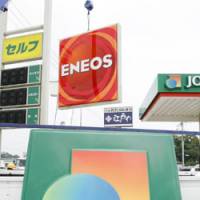 High-octane competition: A JOMO sign representing Japan Energy Corp. is taken off for replacement by an ENEOS sign from Nippon Oil Corp. at a gas station in Saitama Thursday. The two companies have merged and integrated their gas station brands. | KYODO PHOTO