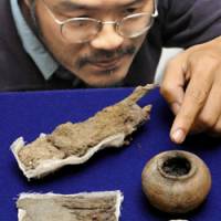 Rare find: Masahiro Ikeda, curator at the Hyogo Prefectural Museum of Archaeology, points Wednesday to a pot from an ancient makeup kit discovered in a tomb in Nishiwaki, Hyogo Prefecture. Above left is a rusty clod in which a pair of iron scissors and tweezers are embedded. Also in the picture is a Chinese bronze mirror. | KYODO PHOTO