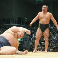 Last man standing: Ama stands over Kotomitsuki after beating the ozeki at the Kyushu Grand Sumo Tournament on Saturday to maintain a share of the lead with yokozuna Hakuho going into the final day. | KYODO PHOTO