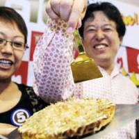 Worth its weight in gold: A man points to a Mido-Suji \"okonomiyaki\" pancake with a pure gold \"teko\" spatula in Kita Ward, Osaka, on Oct. 6. The pancake was the winning recipe in Yukari\'s Teko-1GP contest seven years ago. | KYODO PHOTO