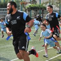 Child\'s play: All Blacks Charlie Faumuina (left) and Dan Carter take part in a touch rugby game with children during their visit to a Tokyo elementary school on Friday. | AFP-JIJI