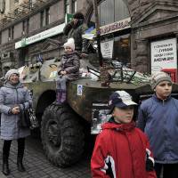 Children stand in front of an armored vehicle, formerly used by Ukraine’s security forces, in Kiev on Monday. | AFP-JIJI