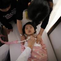 A doctor conducts a thyroid examination on 5-year-old girl as her older brother and a nurse take care of her at a clinic in temporary housing complex in Nihonmatsu, west of the tsunami-crippled Fukushima No. 1 nuclear power plant, on Feb. 27.  | AFP-JIJI