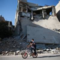 Boys ride a bicycle near rubble of damaged buildings in Douma, near Damascus, Monday. | REUTERS