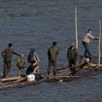 North Korean men ride a makeshift raft made of fastened logs down the Yalu river that divides North Korea from the Chinese border town of Linjiang in northeastern China's Jilin province in August. North Korea is changing, quietly but powerfully, with the rise of the young ruler Kim Jong Un extending even to those secret trails, where business has turned bad for the small-time smugglers who long dominated the border. | AP