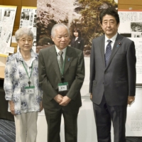 Abe poses with the parents of abductee Megumi Yokota at an exhibition in June 2014.   | KYODO